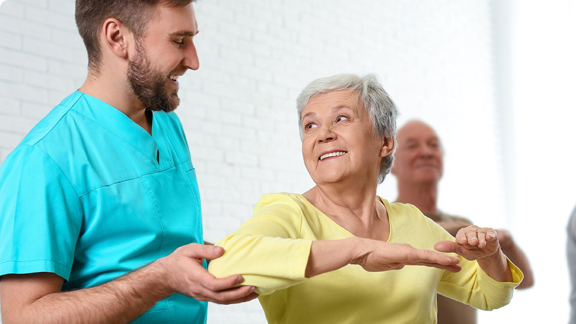 Male health care professional providing exercise assistance to elderly female.